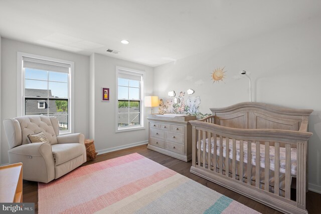 bedroom with wood finished floors, a nursery area, visible vents, recessed lighting, and baseboards