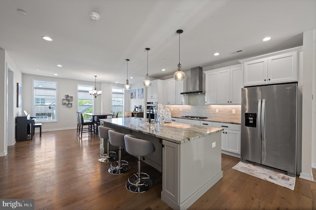 kitchen with visible vents, stainless steel fridge, wall chimney range hood, a center island with sink, and white cabinets