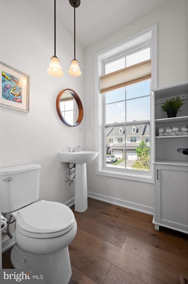 half bath with toilet, baseboards, and wood finished floors