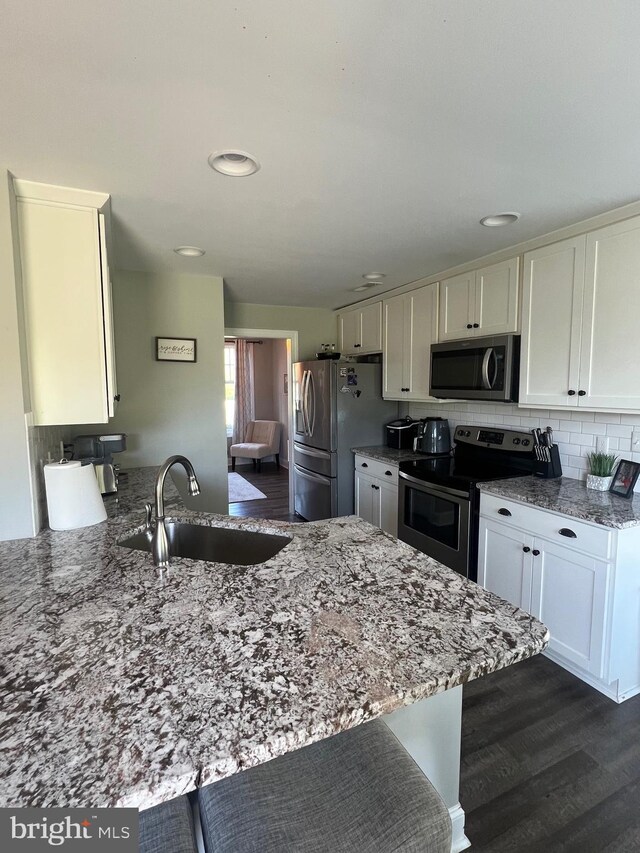 kitchen featuring light stone countertops, white cabinetry, a sink, and appliances with stainless steel finishes