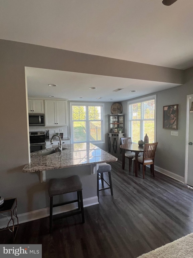 kitchen with a sink, stainless steel microwave, white cabinetry, stove, and light stone counters