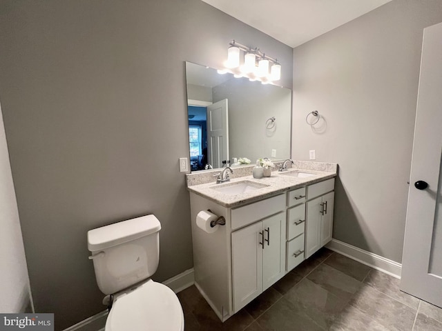 bathroom featuring double vanity, baseboards, a sink, and toilet