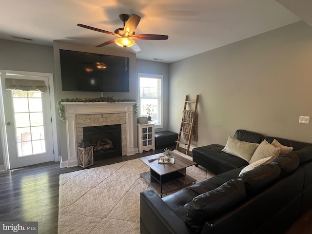 living area featuring ceiling fan, a fireplace, visible vents, wood finished floors, and baseboards