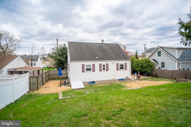 back of property with a yard, central air condition unit, a fenced backyard, and a shingled roof
