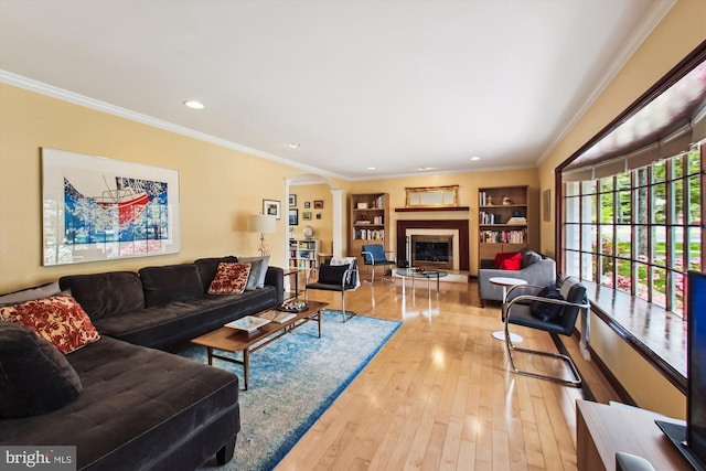 living room featuring light wood finished floors, built in features, recessed lighting, a fireplace with raised hearth, and ornamental molding