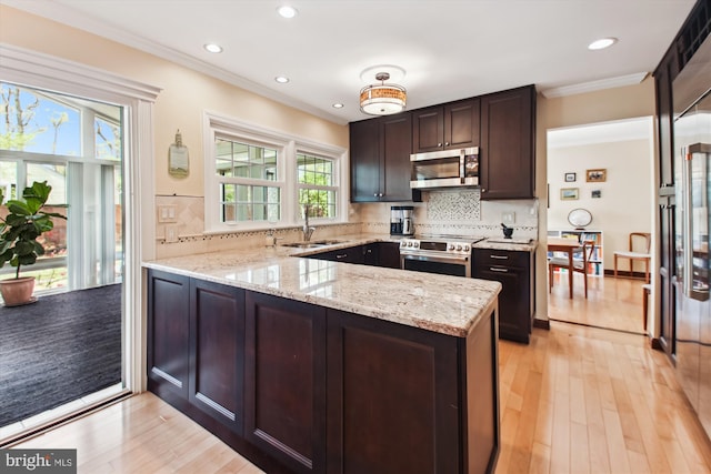 kitchen featuring a sink, appliances with stainless steel finishes, a peninsula, ornamental molding, and light stone countertops