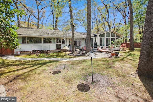 rear view of house with a sunroom, fence, a yard, and a patio