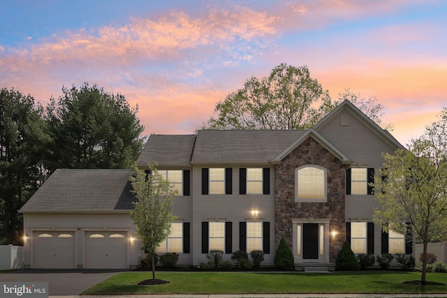 colonial-style house with driveway, a front yard, an attached garage, and stone siding