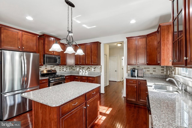 kitchen with a sink, stainless steel appliances, light stone counters, backsplash, and dark wood finished floors