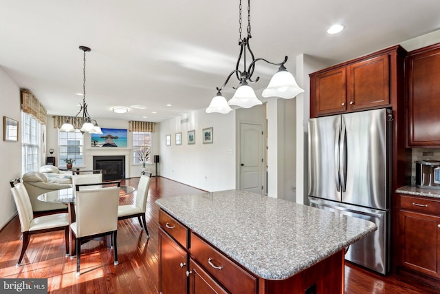 kitchen featuring a kitchen island, dark wood-style floors, freestanding refrigerator, a glass covered fireplace, and a notable chandelier