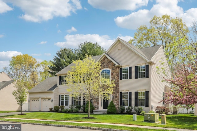 colonial inspired home with a front lawn, stone siding, an attached garage, and aphalt driveway