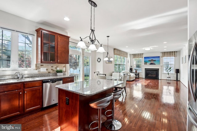 kitchen featuring stainless steel appliances, a glass covered fireplace, a center island, a sink, and dark wood-type flooring