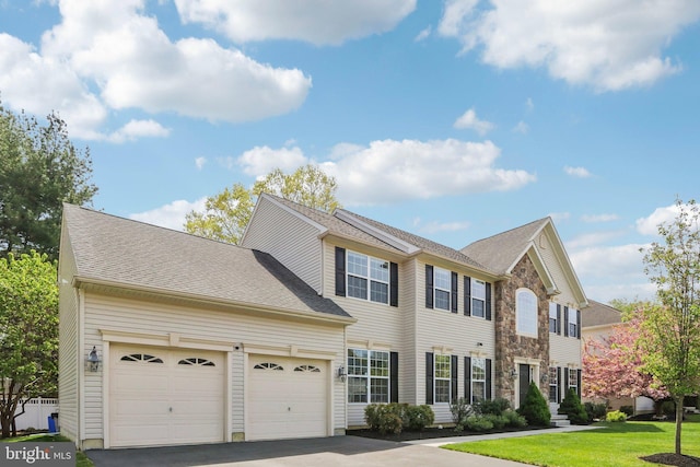 colonial house featuring driveway, a front yard, a shingled roof, and an attached garage