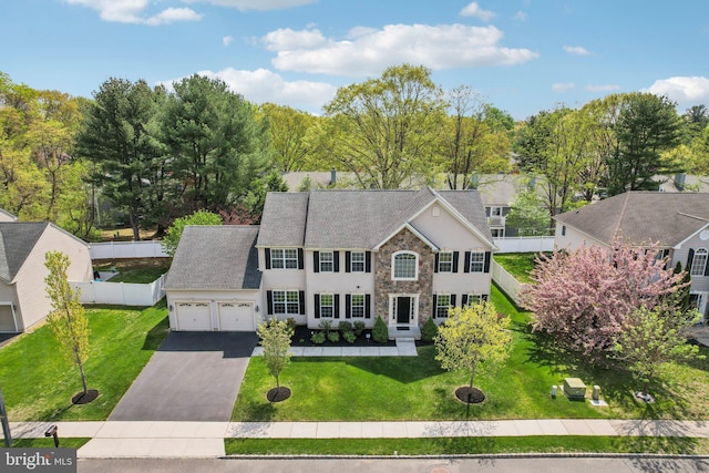 colonial-style house with a garage, aphalt driveway, a front lawn, and stone siding
