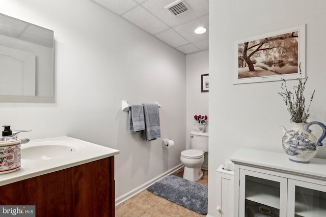 bathroom featuring toilet, vanity, baseboards, visible vents, and a paneled ceiling