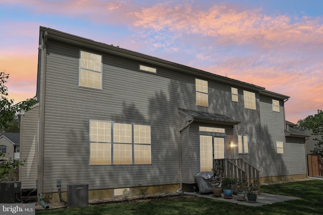 back of property at dusk featuring a yard and central AC
