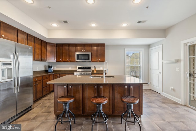 kitchen featuring appliances with stainless steel finishes, a sink, visible vents, and dark stone countertops