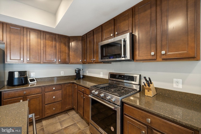kitchen featuring tile patterned flooring, stainless steel appliances, and dark stone countertops
