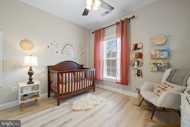 bedroom with visible vents, wood finished floors, baseboards, ceiling fan, and a nursery area
