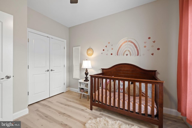 bedroom with a closet, wood finished floors, baseboards, a crib, and a ceiling fan