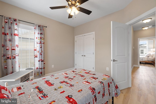 bedroom with baseboards, a ceiling fan, a closet, and light wood-style flooring