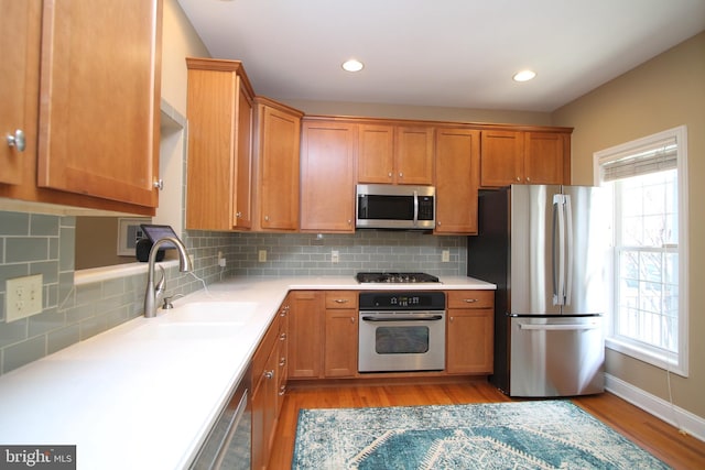 kitchen with light countertops, backsplash, a sink, light wood-style floors, and appliances with stainless steel finishes