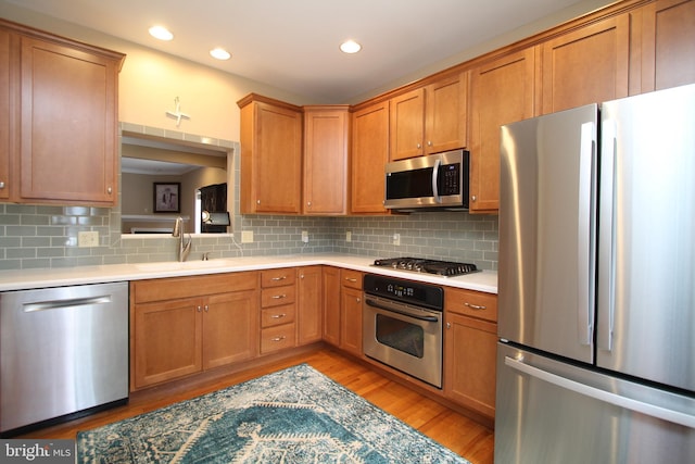 kitchen featuring a sink, light countertops, light wood-style flooring, backsplash, and appliances with stainless steel finishes