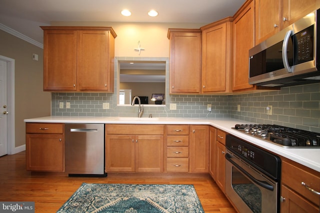 kitchen with light wood-style floors, crown molding, stainless steel appliances, and a sink