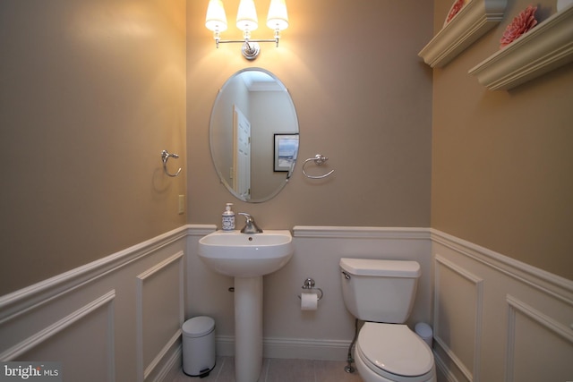 half bath with a decorative wall, toilet, a sink, and wainscoting