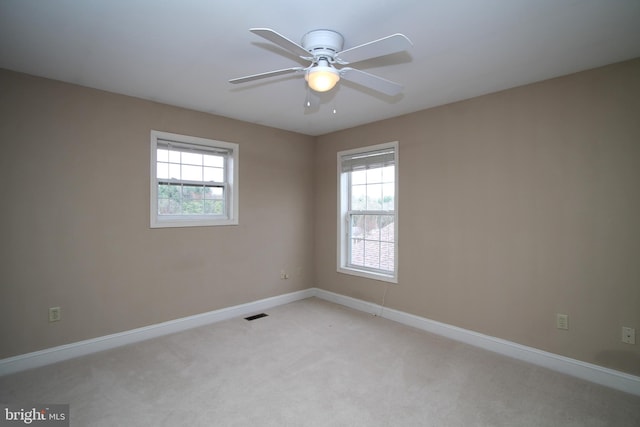 empty room featuring plenty of natural light, light carpet, visible vents, and a ceiling fan