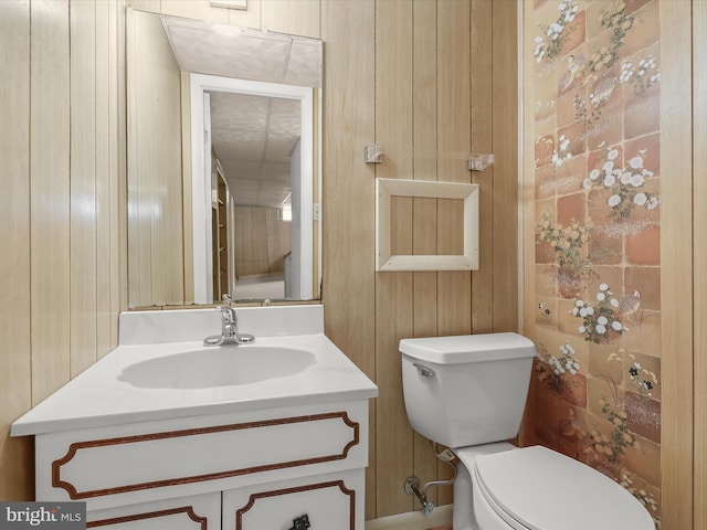 half bathroom with toilet, wood walls, and vanity