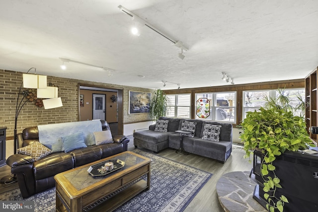living room featuring track lighting, brick wall, and wood finished floors