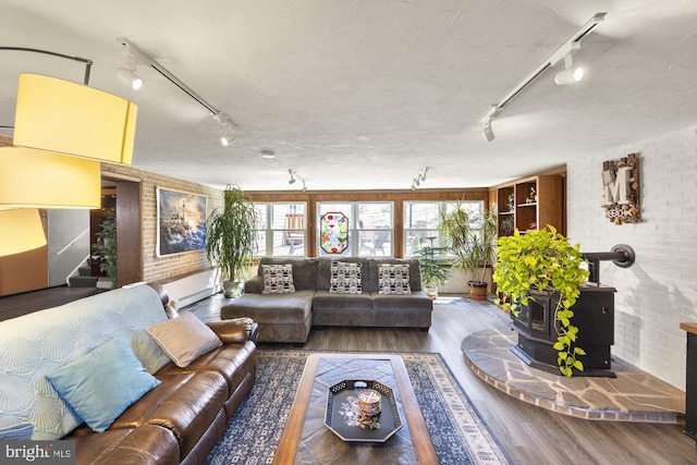 living room with a baseboard heating unit, rail lighting, a wood stove, and wood finished floors