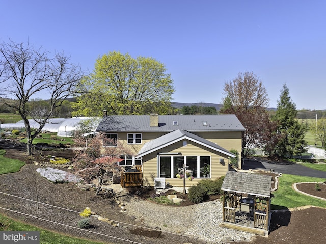 back of house featuring a chimney and metal roof
