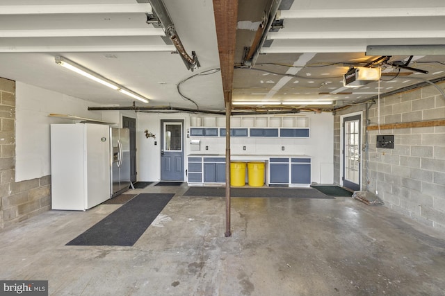 garage with concrete block wall, white fridge with ice dispenser, stainless steel fridge, and a garage door opener