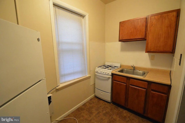 kitchen with light countertops, a sink, white appliances, and baseboards