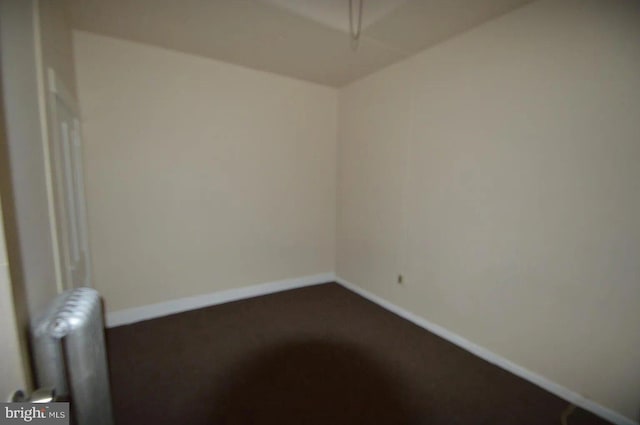 unfurnished room featuring dark carpet, radiator heating unit, and baseboards