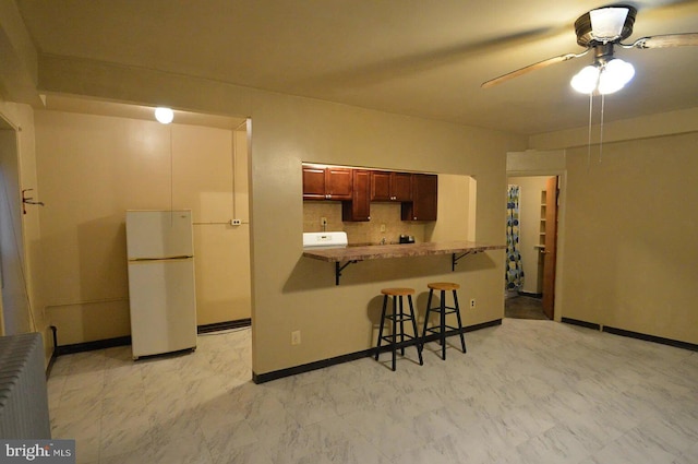kitchen with baseboards, freestanding refrigerator, a breakfast bar, a ceiling fan, and radiator heating unit
