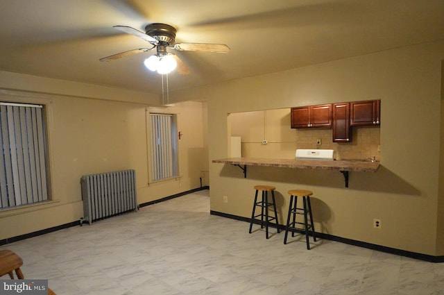 kitchen with baseboards, a kitchen breakfast bar, a peninsula, a ceiling fan, and radiator