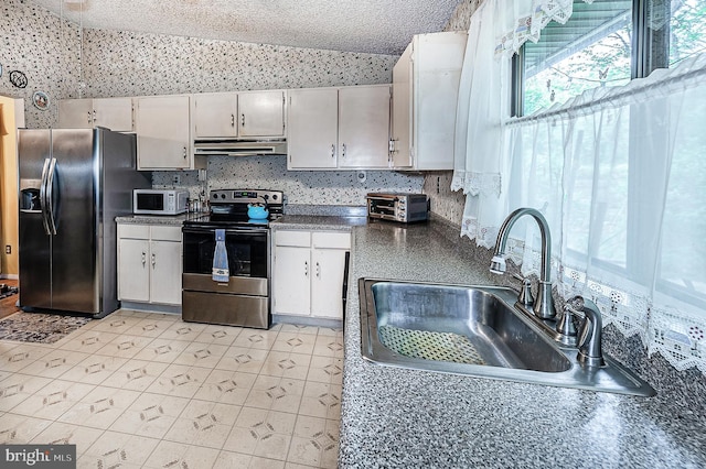 kitchen with stainless steel appliances, under cabinet range hood, a sink, dark countertops, and wallpapered walls