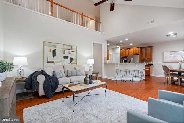 living area featuring wood finished floors, visible vents, baseboards, high vaulted ceiling, and ceiling fan