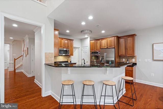 kitchen with a peninsula, dark wood-style flooring, appliances with stainless steel finishes, and tasteful backsplash