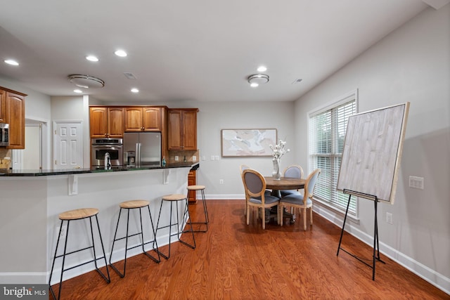 kitchen featuring stainless steel appliances, dark wood finished floors, dark countertops, baseboards, and a kitchen bar