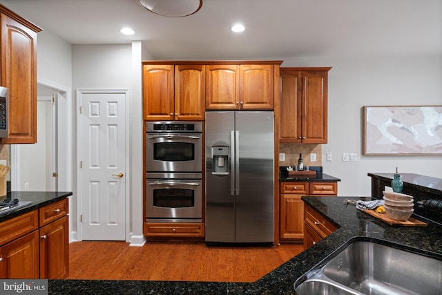 kitchen with dark stone counters, dark wood finished floors, brown cabinets, and appliances with stainless steel finishes