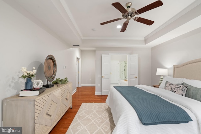bedroom with wood finished floors, a tray ceiling, baseboards, ornamental molding, and visible vents