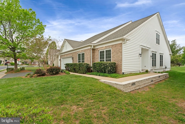 view of side of property with a lawn, brick siding, roof with shingles, and a garage