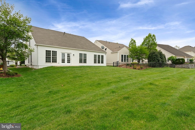 rear view of house with a yard, a shingled roof, and fence
