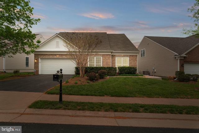 view of front facade with aphalt driveway, a yard, central AC, an attached garage, and brick siding