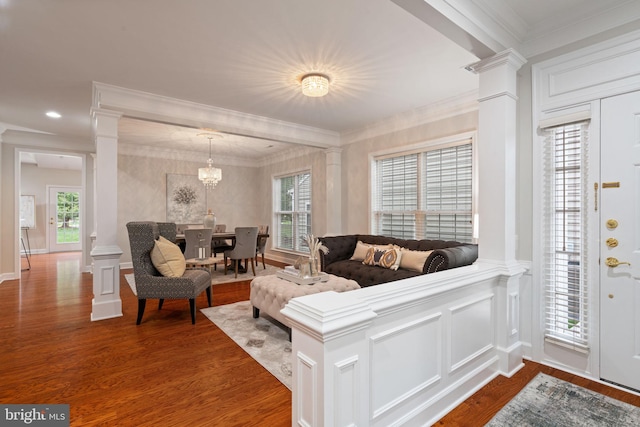 living area with wood finished floors, a decorative wall, ornamental molding, and decorative columns
