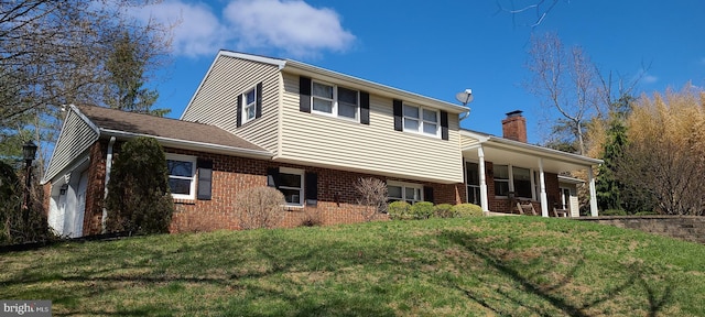 view of front of property featuring a front yard, a chimney, covered porch, and brick siding